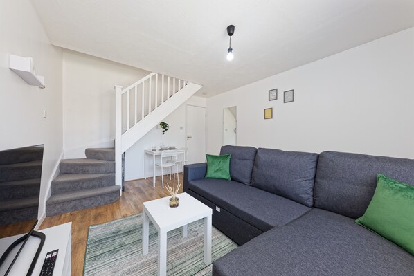 A modern living room with a grey sofa, white coffee table, and a staircase.