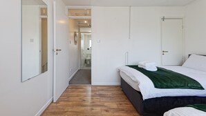 A bedroom with a bed, a mirror, and a door leading to a bathroom. - Lovely 2-bed House in Kent - Parking Available (Greenhithe)