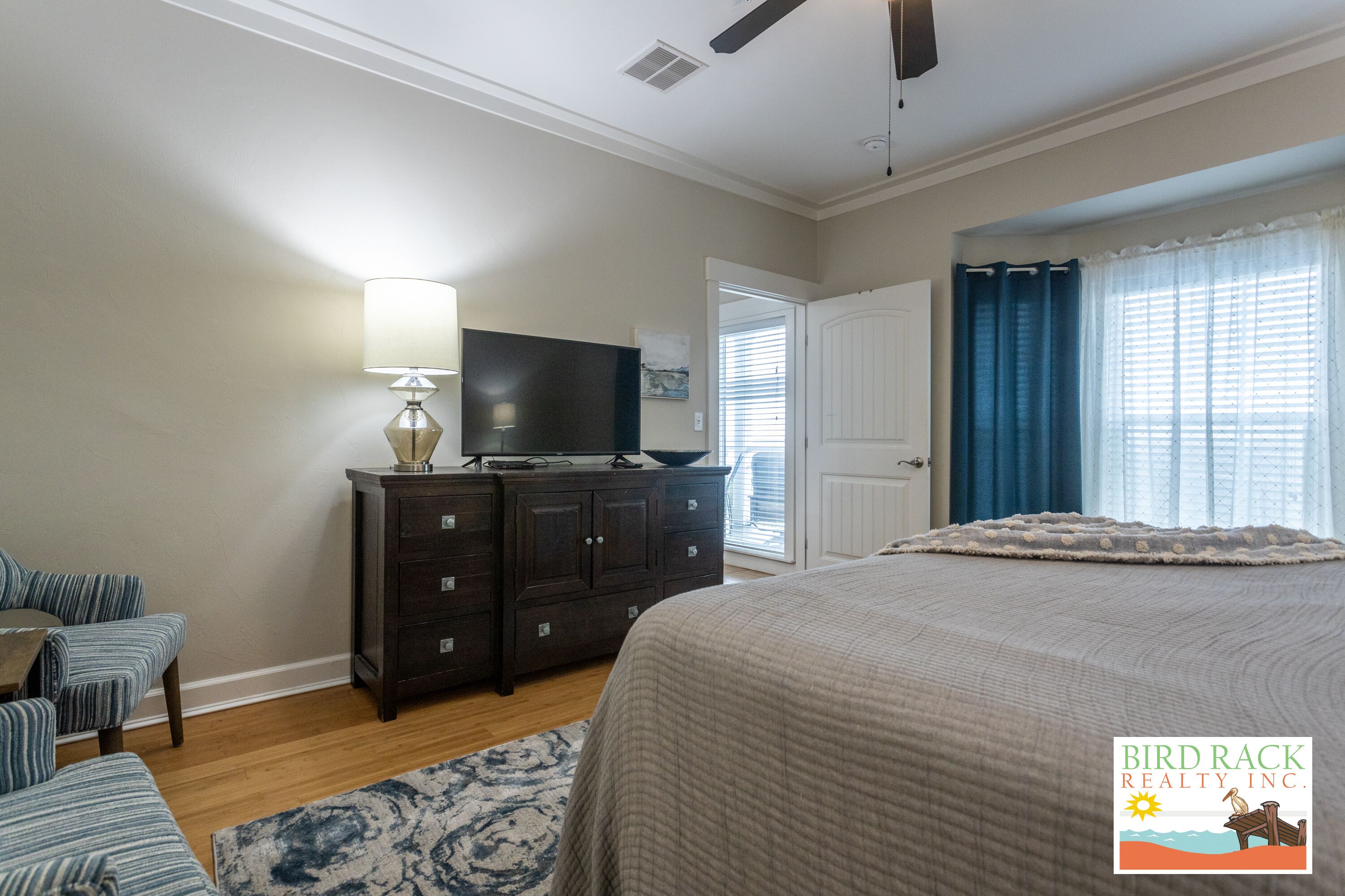 A bedroom with a large bed, a dresser, a television, and a window with curtains.