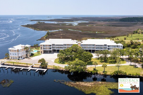 A waterfront property with a large building, a dock, and a grassy area with trees.