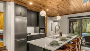 A modern kitchen with a central island, dark cabinets, stainless steel appliances, and a wooden ceiling.