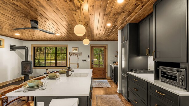 A modern kitchen with a central island, black cabinets, and a wood-paneled ceiling.
