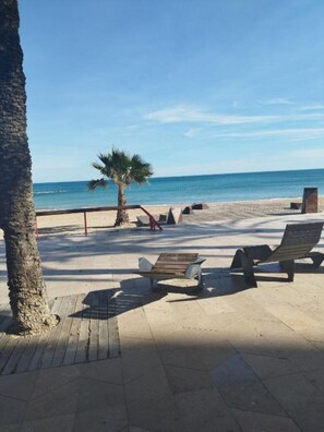 A beachside patio with wooden lounge chairs, a palm tree, and a view of the ocean. - Costa Norte Vinaros (Vinaròs)