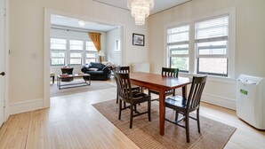 Een ruime eethoek met een houten tafel en stoelen, een kroonluchter en grote ramen met zonwering.
