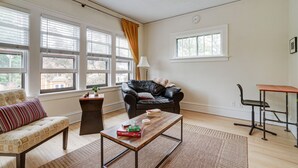 Een woonkamer met een bank, een salontafel, een zwarte lederen fauteuil, een kleine tafel met boeken en een raam met gordijnen.