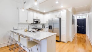 Una cocina moderna con armarios blancos, electrodomésticos de acero inoxidable y una isla central con taburetes de bar.