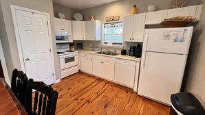 Una cocina compacta con armarios blancos, microondas, estufa, lavavajillas y refrigerador.