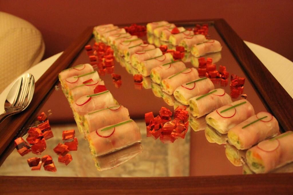 A tray of spring rolls with decorative garnishes on a reflective surface.