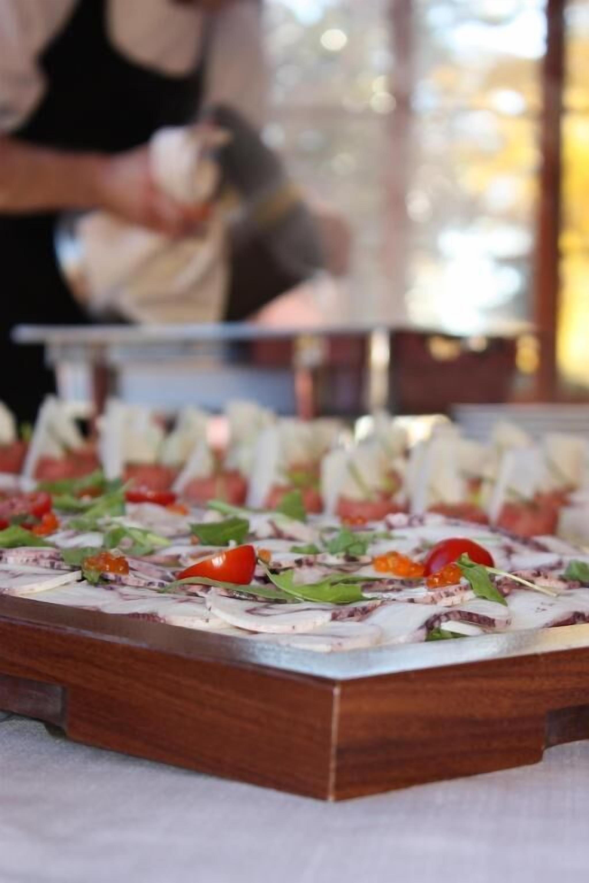 A wooden serving tray with food items, including sliced tomatoes and greens, in a restaurant setting.