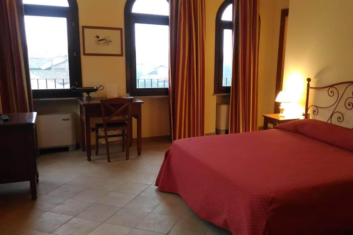 A hotel room with a bed, desk, chair, and a window with curtains.