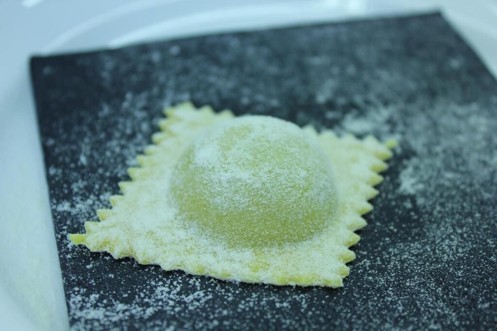 A square plate with a round, dusted food item on a dark surface.