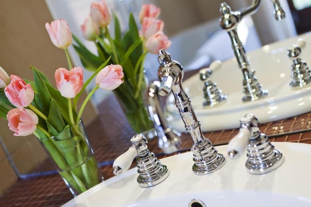 A bathroom sink with antique-style faucets and a vase of pink tulips.