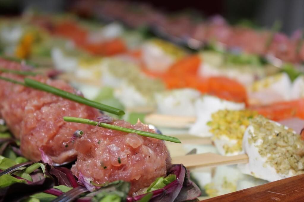 A variety of food items, including a skewered meat dish, possibly sushi, and other prepared foods on a tray.