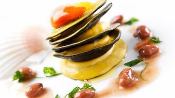Prato de frutos do mar com mexilhões, tomates cereja e ervas sobre um prato branco.