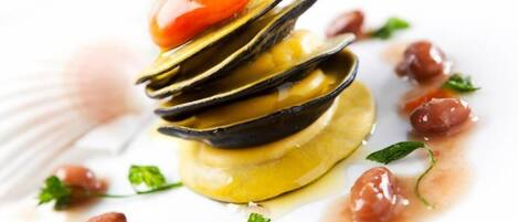 A seafood dish with mussels, cherry tomatoes, and herbs on a white plate.