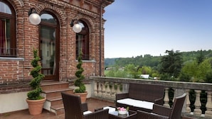 A brick building with a balcony, furnished with wicker chairs and a table, overlooking a green landscape. - Villa Soleil  (Colleretto Giacosa)