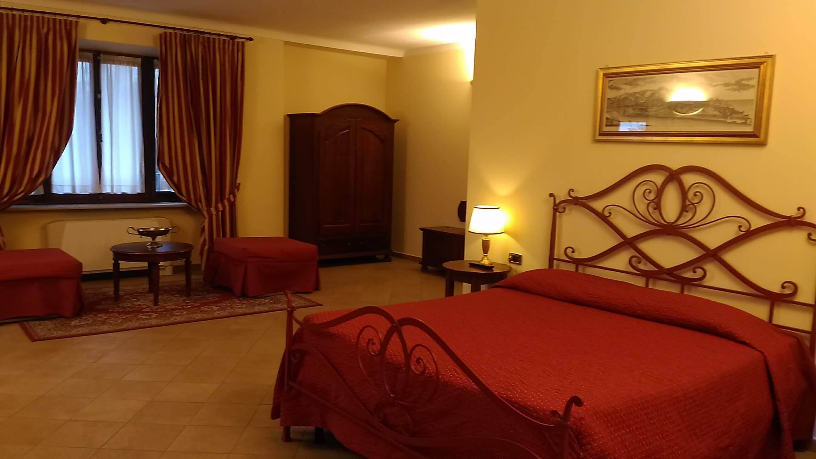 A hotel room with a bed, a desk, a chair, a wardrobe, and a painting on the wall.