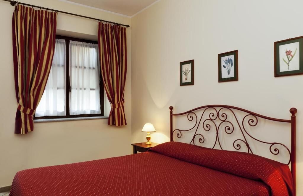 A bedroom with a bed, curtains, a nightstand with a lamp, and three framed pictures on the wall.
