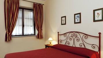 A bedroom with a bed, curtains, a nightstand with a lamp, and three framed pictures on the wall.