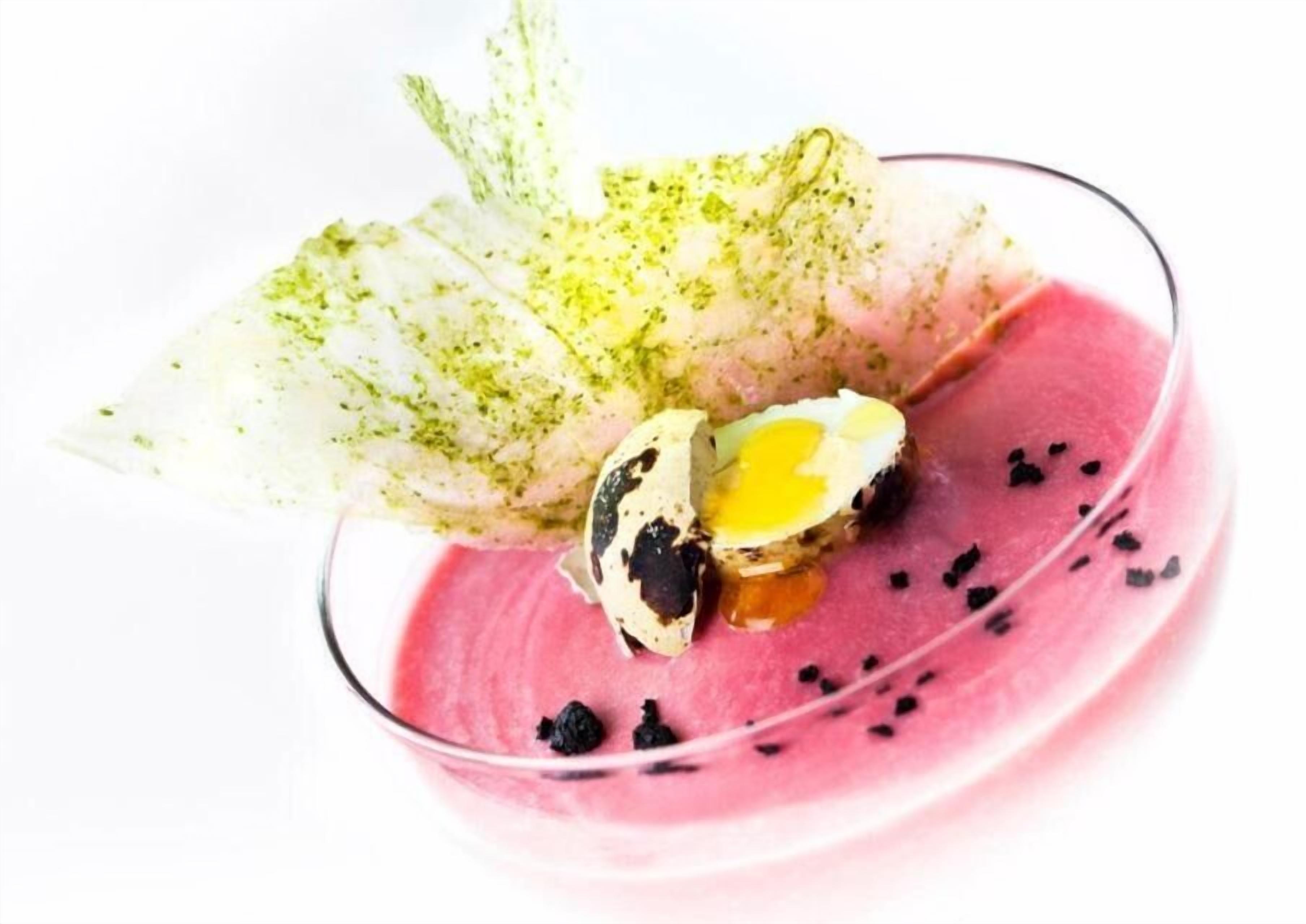 A dessert with a pink base, a green leaf garnish, and a cracked egg yolk.