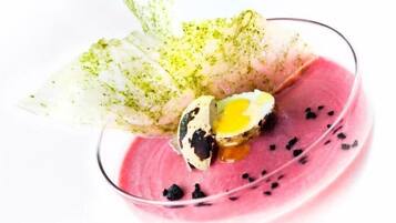 A dessert with a pink base, a green leaf garnish, and a cracked egg yolk.