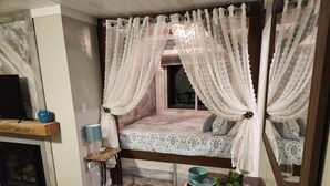 Una camera da letto accogliente con un letto, un comodino, una lampada e una finestra con tende leggere.