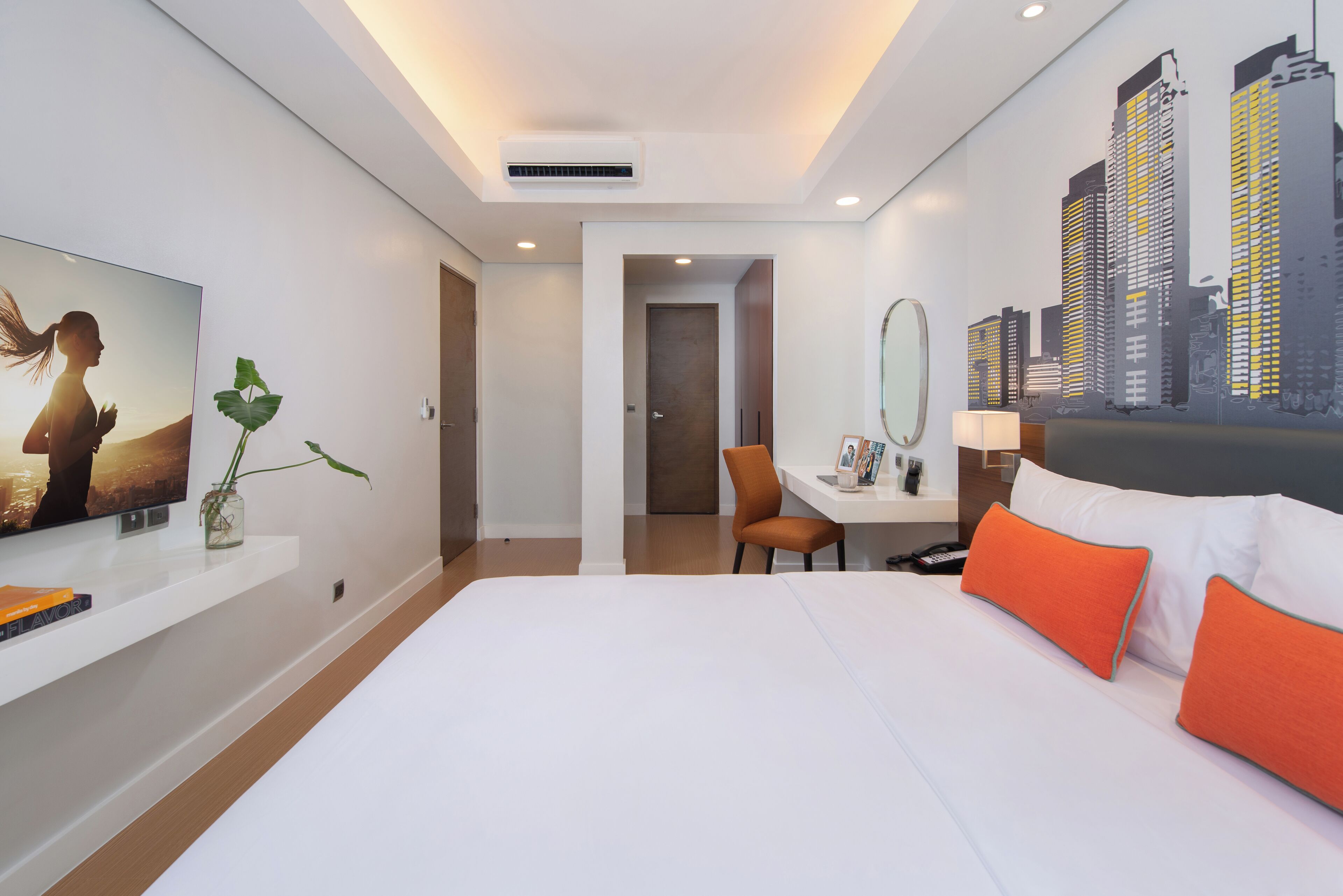 Una habitación de hotel moderna con una cama grande, un escritorio, una silla, un televisor y un mural con vista a la ciudad.