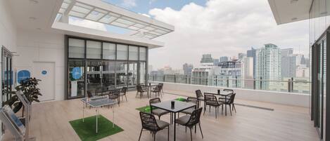A modern rooftop terrace with a city view, furnished with tables and chairs, and a ping pong table.