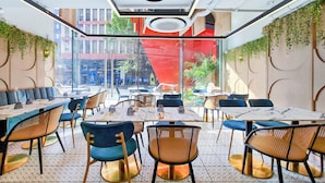 A restaurant with a modern interior, featuring tables and chairs, a ceiling light, and a large window with a view of the street. - Citadines Benavidez Makati (Makati)