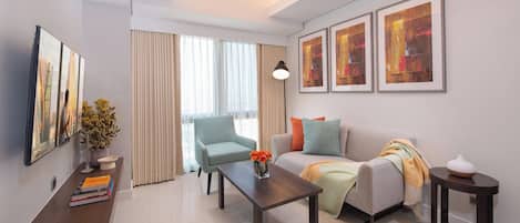 Una sala de estar moderna con un sofá, un sillón, una mesa de centro y una mesita auxiliar. Hay obras de arte enmarcadas en la pared y un jarrón con flores sobre una consola.
