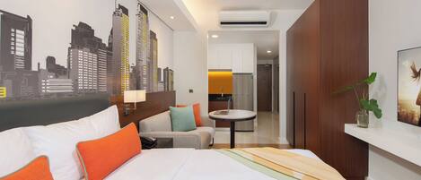 Una habitación de hotel moderna con cama, sofá, zona de comedor y un mural de paisaje urbano en la pared.