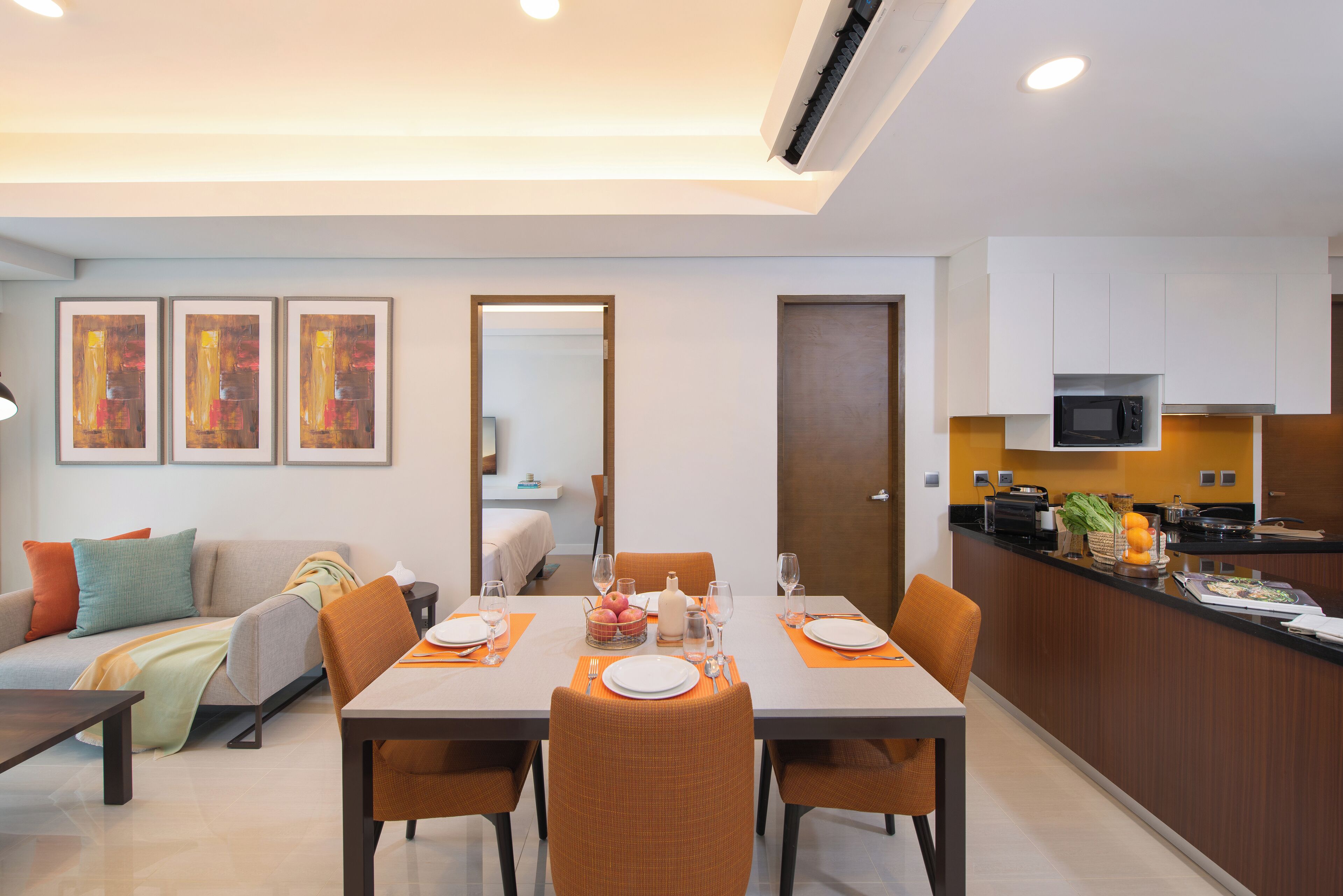 A modern dining area with a table set for four, a sofa, and a kitchen area with a microwave.