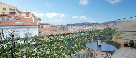 A terrace with a table and chairs, a bottle of wine, and potted plants.