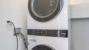 Un appareil combiné lave-linge et sèche-linge, de type « empilable », avec un câble d’alimentation et un panneau de commande visibles.
