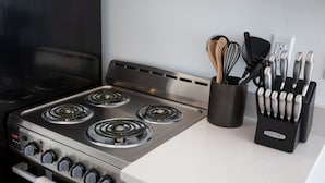 Une cuisine équipée d’une cuisinière en acier inoxydable, d’un bloc à couteaux et d’un plan de travail blanc.