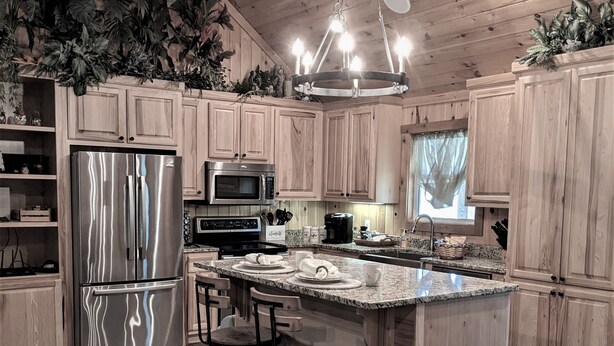 A modern kitchen with wooden cabinets, stainless steel appliances, a granite countertop, and a central island with bar stools.
