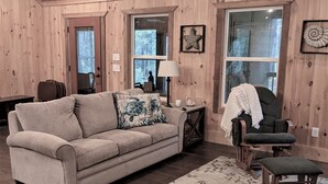 A cozy living room with a beige sofa, a patterned rug, and wooden walls.