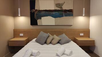 A neatly made bed with white linens and two towels, a headboard with a painting, and two bedside tables with lamps.