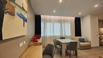 Uma sala de estar moderna com área de jantar, uma pintura grande na parede e uma janela com cortinas.