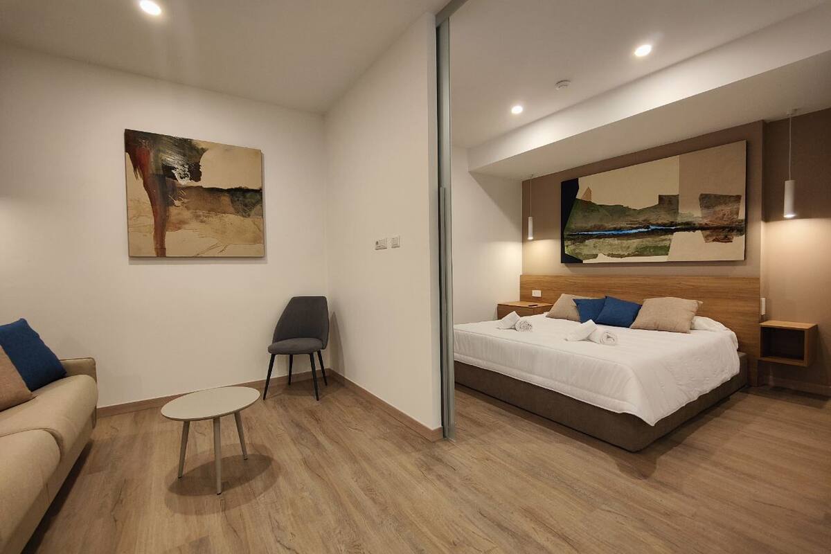 A modern hotel room with a bed, a chair, a small table, and artwork on the walls.