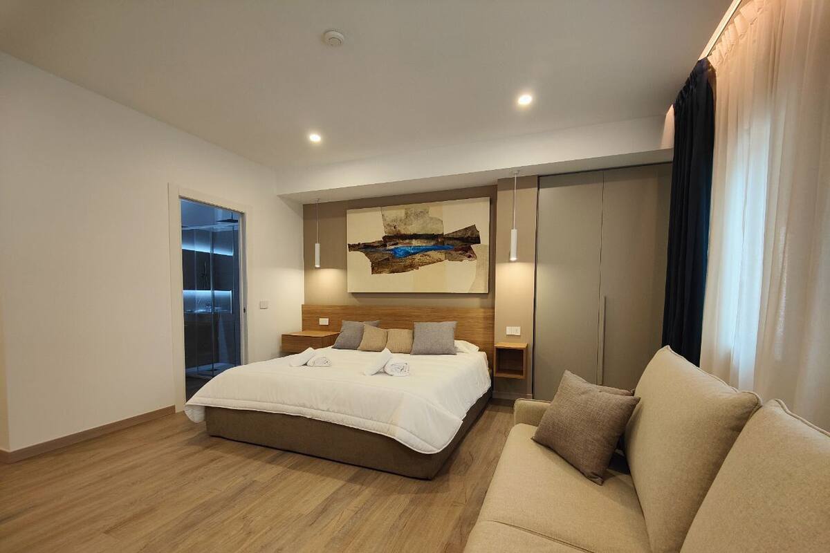 A modern hotel room with a large bed, a sofa, and a wall-mounted artwork.