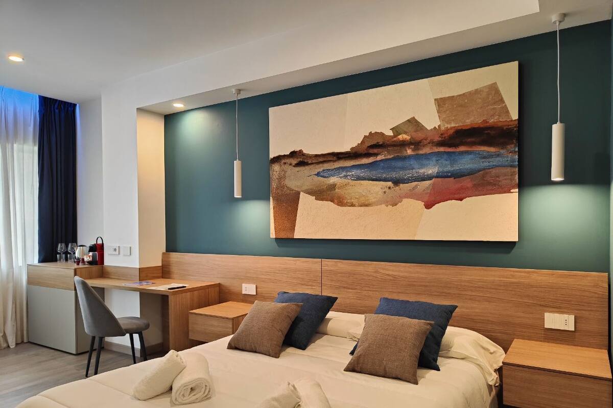 A modern hotel room with a large bed, a desk, and a painting on the wall.