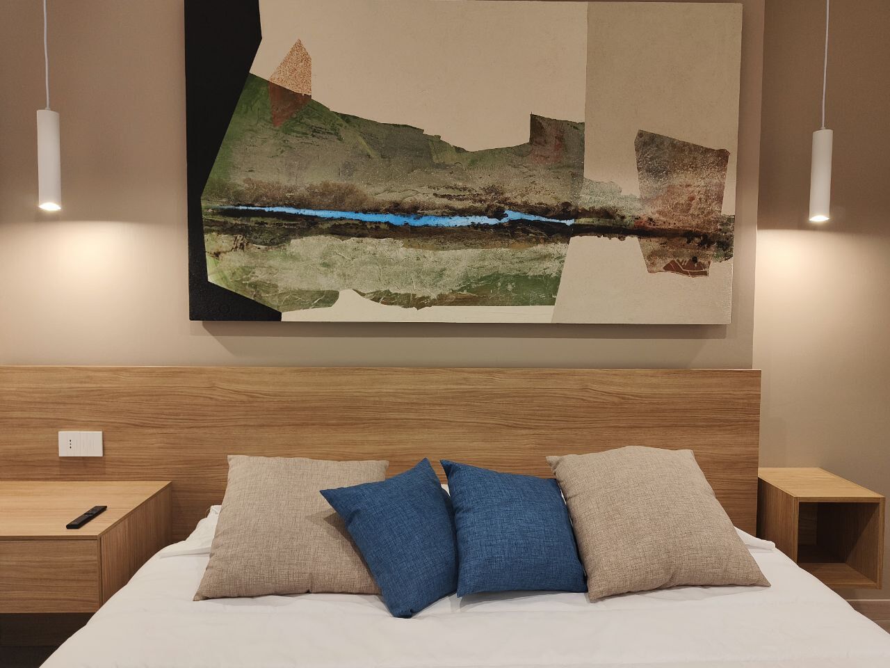 Ein modernes Schlafzimmer mit einem Holzkopfteil, einem großen abstrakten Gemälde und zwei Nachttischen mit Lampen.