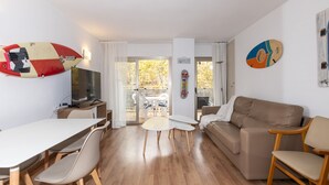A modern living room with a sofa, a dining table with chairs, a TV, and a surfboard decoration.