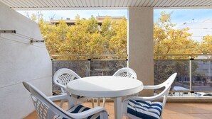 A balcony with a white table and chairs, a view of trees and buildings, and a tiled floor.