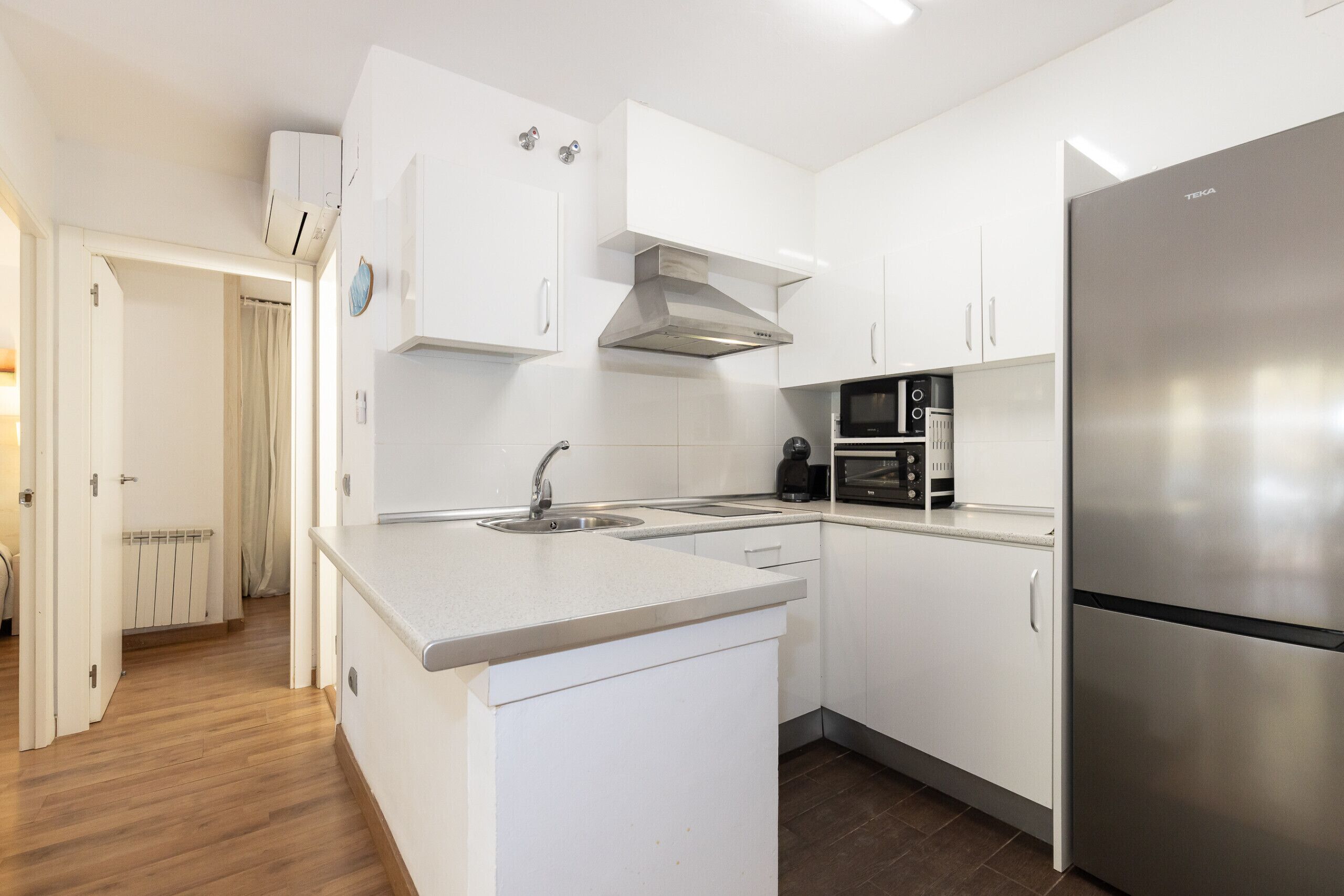 Een moderne keuken met witte kastjes, een roestvrijstalen koelkast, een ingebouwde magnetron en een gasfornuis.