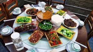 A round dining table with various dishes and bowls of food, surrounded by chairs.