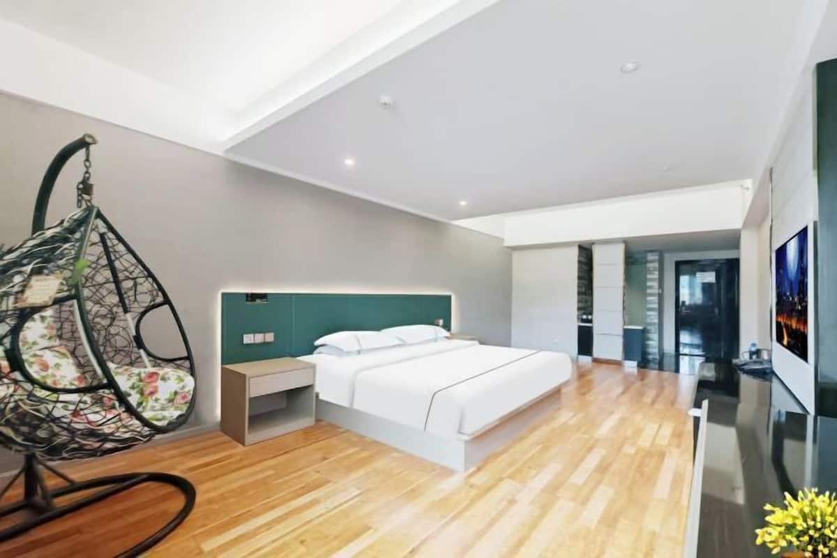A modern hotel room with a bed, a hanging chair, a TV, and a wooden floor.