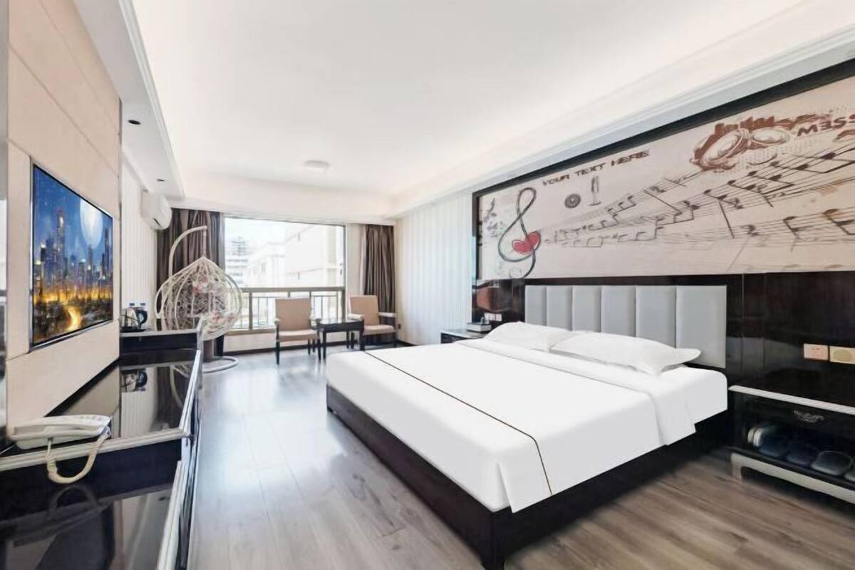 A modern hotel room with a large bed, a desk with a phone, a chair, and a balcony with a view.