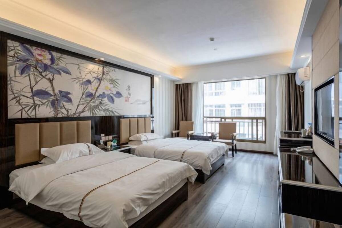 A hotel room with two beds, a TV, a desk, and a large window.